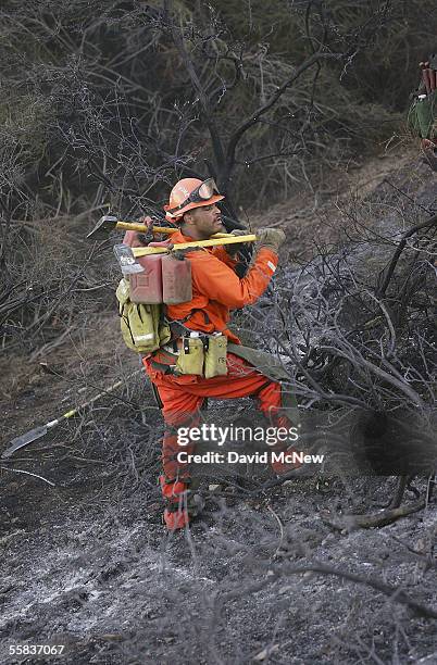 An inmate pauses while carrying gasoline for chain saws up a charred hillside while cutting a fireline around the Castaways Fire on October 1, 2005...