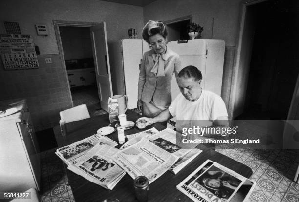 American political activist Phyllis Schlafly, dressed in a suit with a large bow, stands and reads the front page of the St. Louis Globe-Democrat...