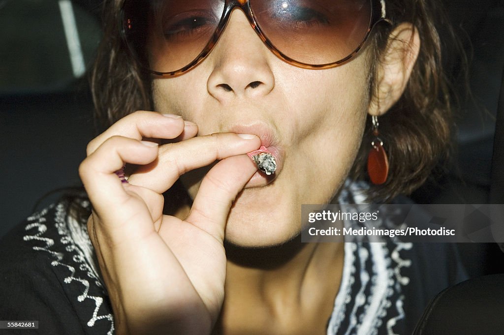 Close-up of young woman in sunglasses smoking a marijuana joint