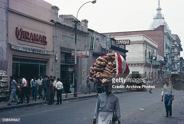 Man using his head to carry chipa in Asunción, Paraguay, circa 1960.