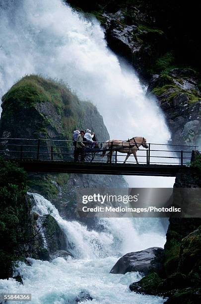 tourist crossing a waterfall in a horse cart on a footbridge, olden, norway - olden foto e immagini stock