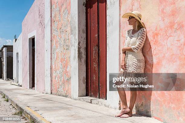 woman with sun hat on leaning against wall - mujeres hot stock-fotos und bilder