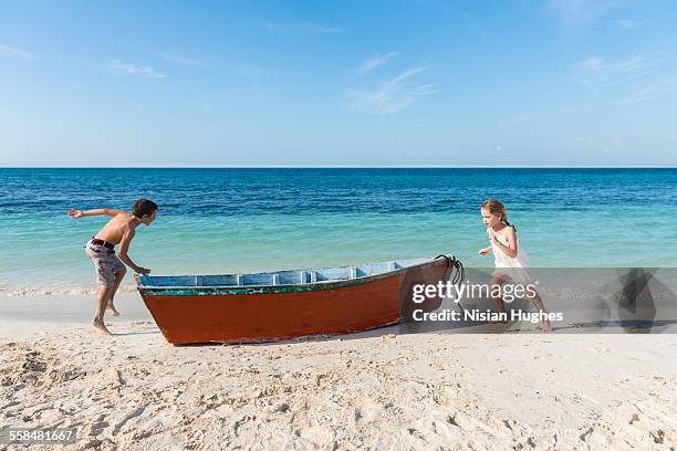 two kids playfully running around small boat - mujeres hot stock-fotos und bilder