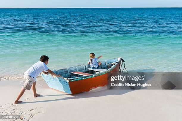 boy pushing small boat with little girl into ocean - mujeres hot stock-fotos und bilder