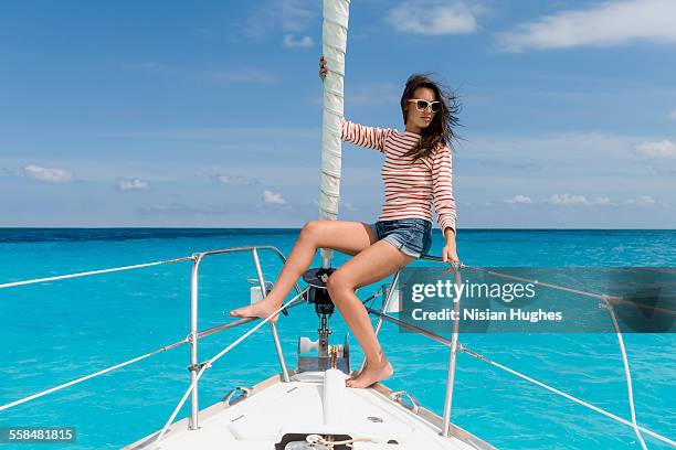 young woman sitting at the bow of sailboat - mujeres hot stock-fotos und bilder