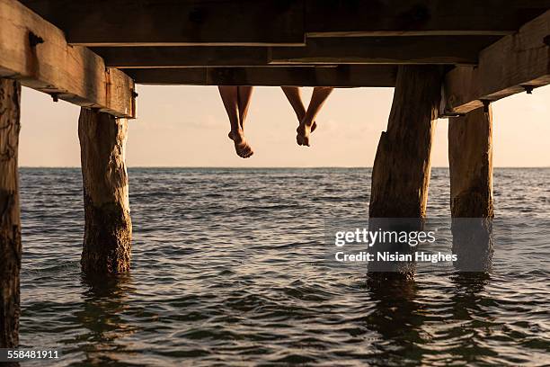 couple's feet dangle from end of pier - mexico sunset stock pictures, royalty-free photos & images