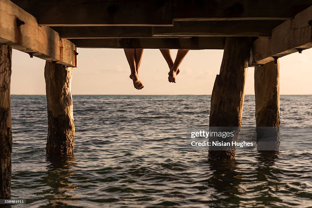 Couple's feet dangle from end of pier