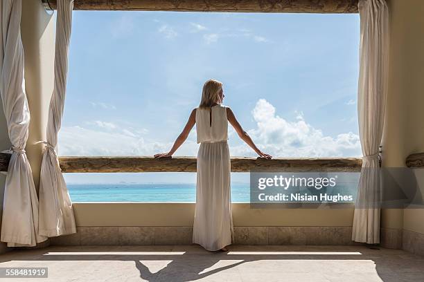woman on balcony looking out at the ocean - femme robe blanche photos et images de collection