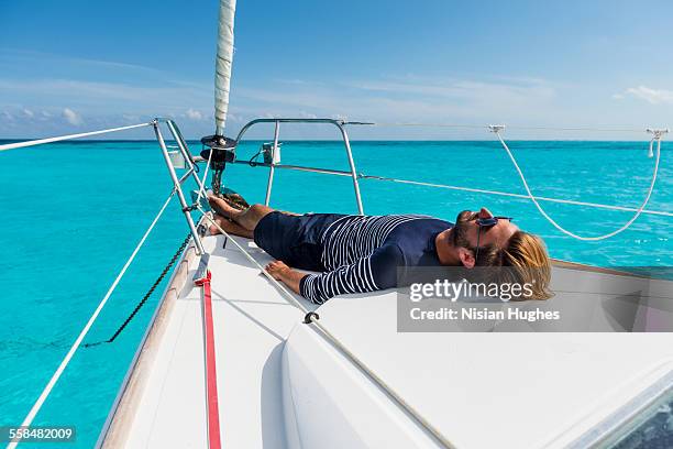 young man laying down at the bow of sailboat - mujeres hot stock-fotos und bilder