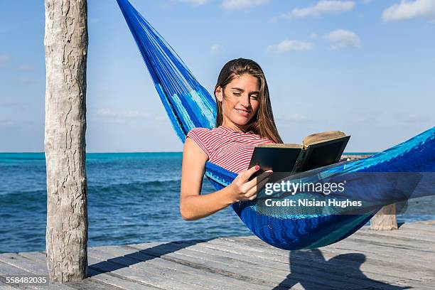 young woman reading book in a hammock - mujeres latinas stock-fotos und bilder