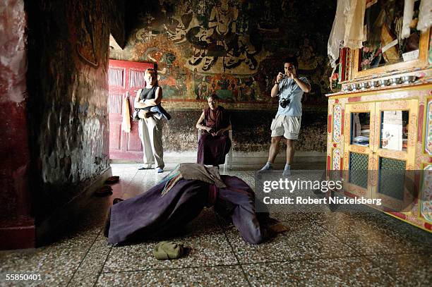 Ladakhi Buddhist woman prostrates herself during prayer as a group of Spanish tourists watch inside the Shey Monastery on August 5, 2005 in Shey,...