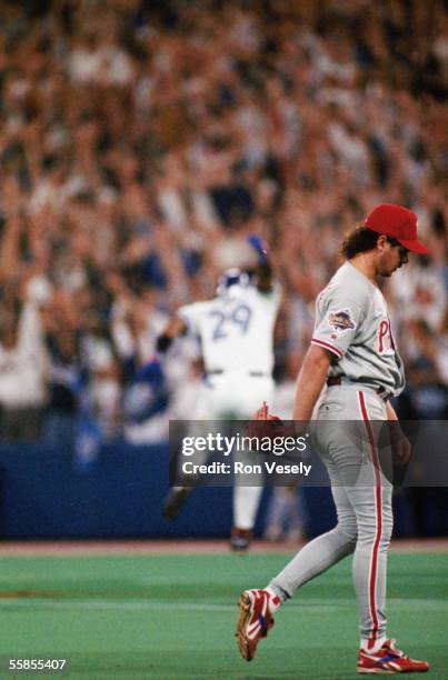 Pitcher Mitch Williams of the Philadelphia Phillies walks off the field as Joe Carter of the Toronto Blue Jays dances his way around the bases after...