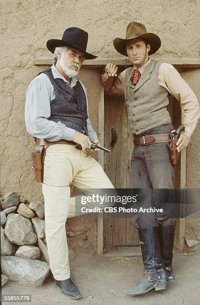 American musician and actor Kenny Rogers holds a pistol in his hand as he stands in character as Brady Hawkes next to colleague and compatriot Brue...