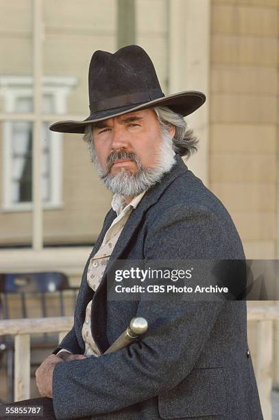 American musician and actor Kenny Rogers sits and holds a walking stick in a publicity photo for the CBS television movie 'The Gambler,' directed by...