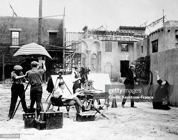 Prise de vue d'un tournage de film, les opérateurs s'apprêtent à tourner, le scénariste est assis, bloc et crayon en main, le metteur en scène montre...