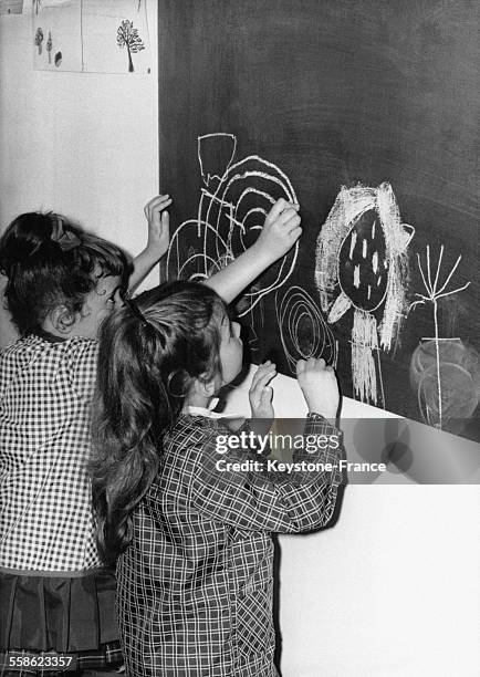 Petites filles dessinant à la craie au tableau lors de la rentrée scolaire en France, le 15 septembre 1967.