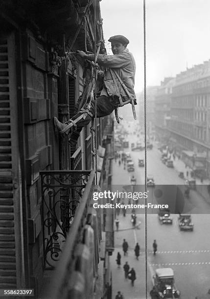 Cet ouvrier qui ravale la façade se balance sur des cordes dans le vide, à Paris, France le 9 mars 1932.