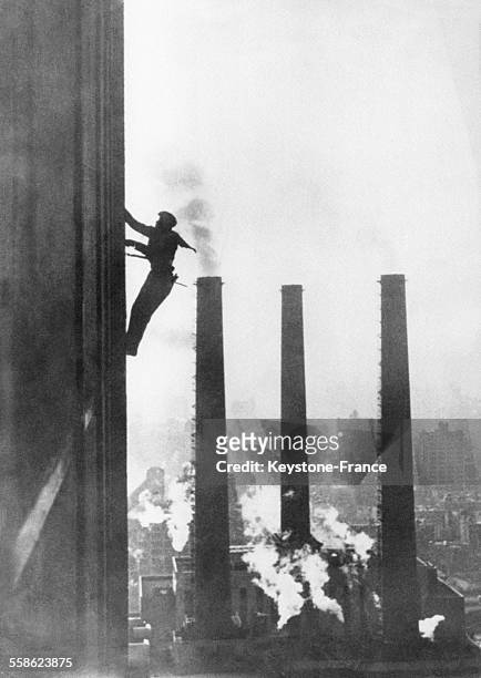 Un laveur de carreaux lave les vitres d'un gratte-ciel devant des cheminées d'usine le 17 septembre 1951 à New York, NY.