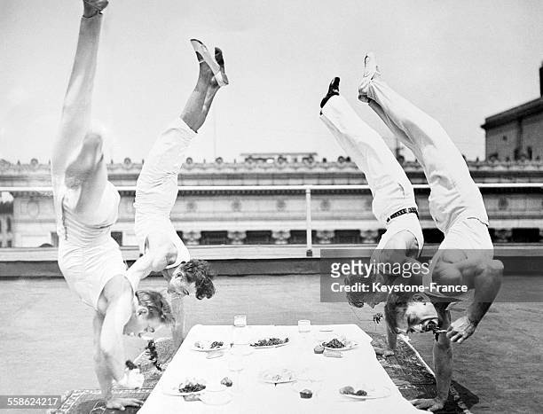 Quatre athlètes déjeunant à leur façon sur le toit d'un gratte-ciel, jambes en l'air et se tenant en équilibre sur la main droite, à Los Angeles,...