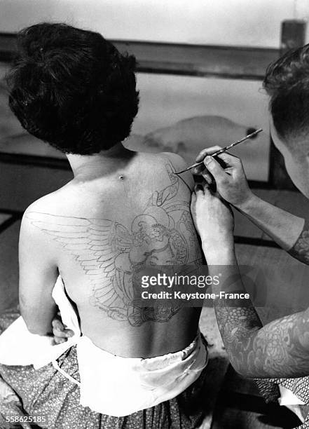 Homme dessinant sur le dos d'une femme avant de la tatouer au Japon en 1950.