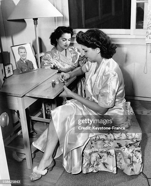 Jeune femme se vernissant les ongles discutant dans sa chambre avec une amie aux Etats-Unis, circa 1940.