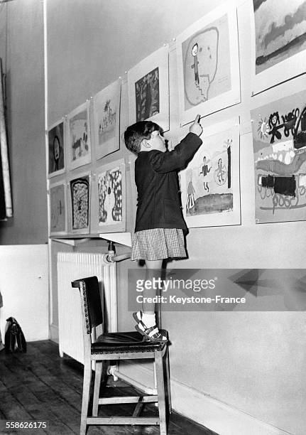 Une enfant accroche son dessin à la 64ème exposition de dessins d'enfants à la Royal Drawing Society à Londres, Royaume-Uni, le 17 avril 1959.