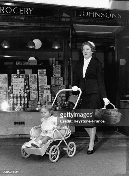 Femme sortant d'un magasin après avoir fait les courses, sa petite fille dans une poussette.