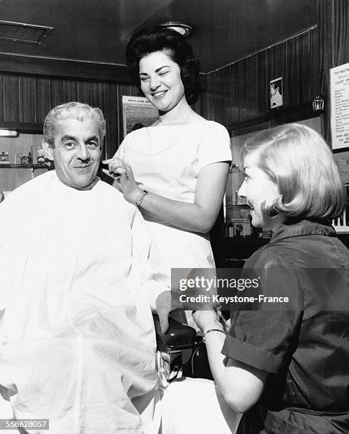 Au Westbury Hotel, Ann Hoffman, la seule femme barbier, rase un client pendant qu'une autre autre jeune femme lui fait la manucre, à Londres,...