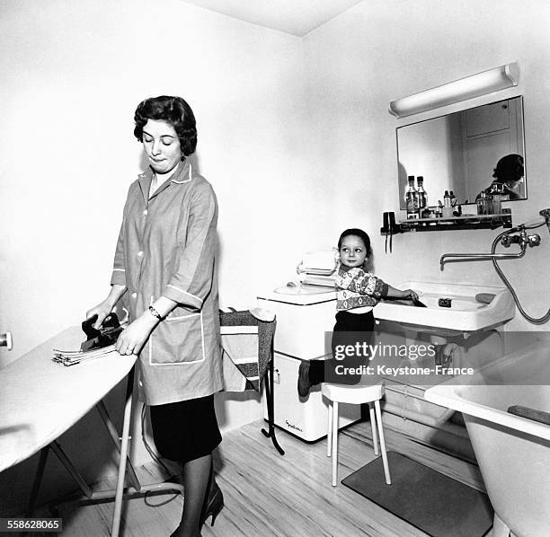 Femme repassant dans la salle de bain pendant que son garçon se lave les mains en 1937.