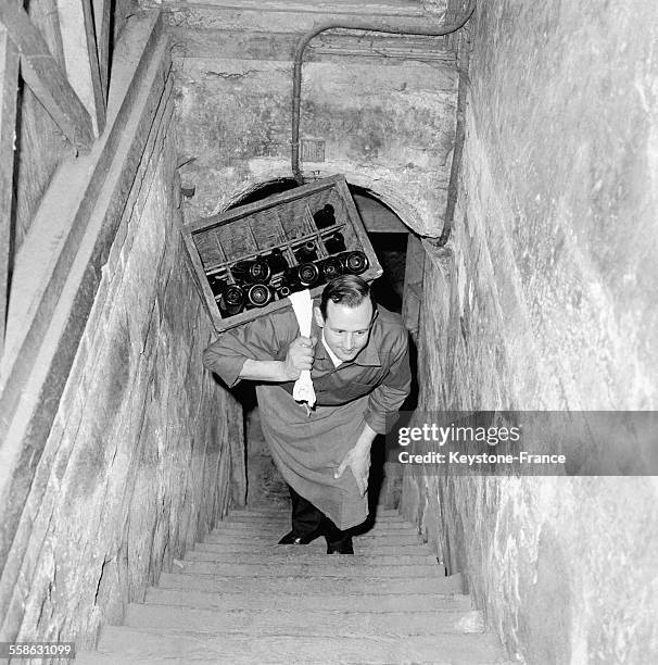 Un homme chargé de bouteilles remonte l'escalier de la cave du restaurant 'Drouant', circa 1960 à Paris, France.