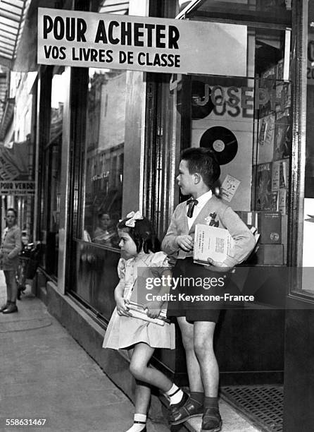 Enfants sortant d'une librairie avec leurs livres scolaires sous le bras, à Paris, France, le 20 septembre 1958.