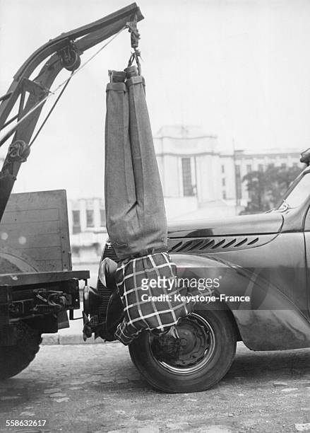 Un mecanicien effectue une reparation automobile en urgence suspendu par les pieds a une poulie, circa 1960 a Paris, France.