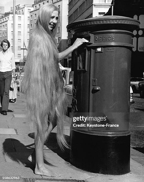 Une femme aux très longs cheveux, qui la couvrent presque entièrement, poste une lettre.