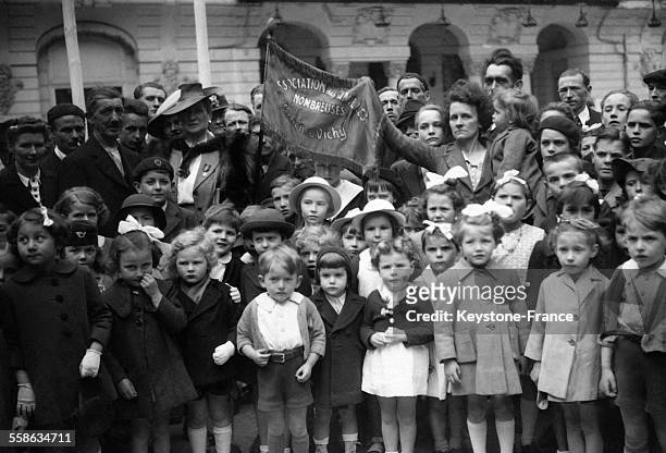 Enfants de familles nombreuses entourant le fanion de leur association pour la fête des mères, en France circa 1940.