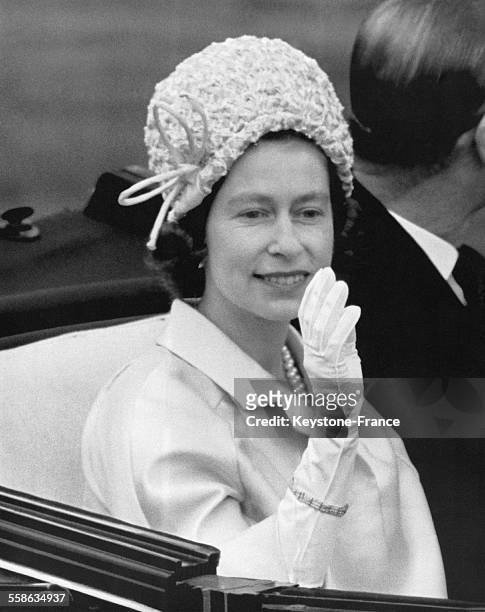 La Reine Elizabeth II salue la foule depuis sa calèche sur le champ de course hippique le 17 juin 1964 à Ascot, Royaume-Uni.