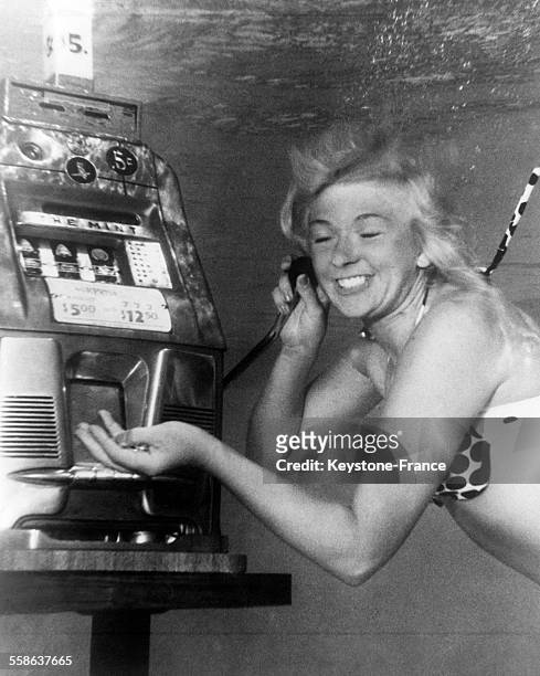 Jeune femme jouant avec une machine à sous installée au fond de la piscine d'un hôtel, à Las Vegas, Nevada, le 24 novembre 1965.