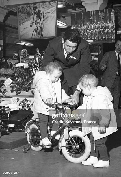 Vendeur faisant essayer une petite bicyclette a des freres jumeaux dans un magasin, France, 28 novembre 1966.