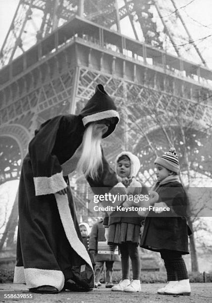 Pere Noel au pied de la Tour Eiffel distribuant des cadeaux aux enfants sur son passage, a Paris, France, le 22 decembre 1960.