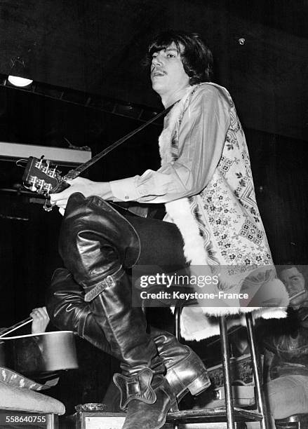 Le chanteur Antoine, cheveux presque courts, vêtu d'une veste hippie et portant d'immenses bottes de mousquetaire, en pleine répétition au cabaret...