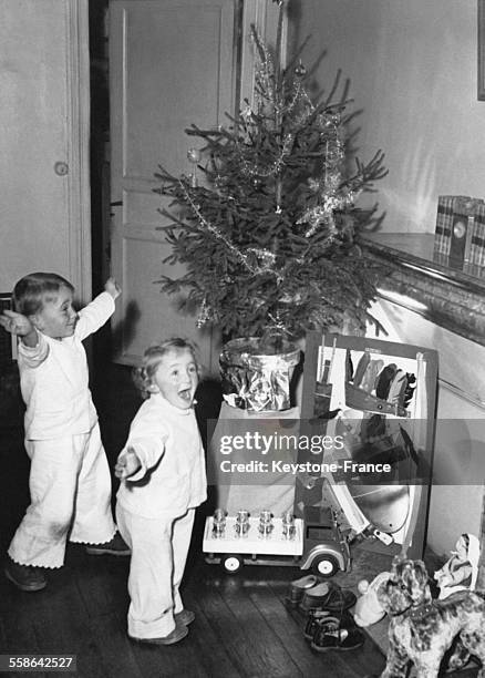 Devant la cheminee d'une famille parisienne, deux enfants manifestent leur joie a la vue de ce que le Pere Noel leur a apporte, le 25 decembre 1952 a...