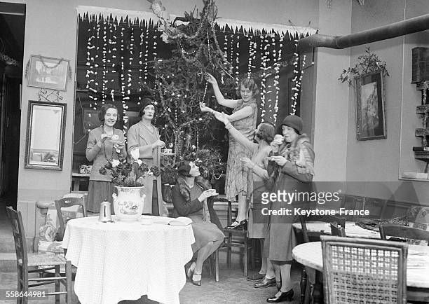 Jeune femme insatallant les décorations de Noël dans un café à Paris, France en décembre 1930.