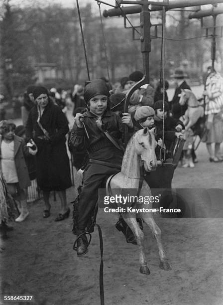 Enfant déguisé sur un cheval de bois, à Paris, France, en mars 1930.