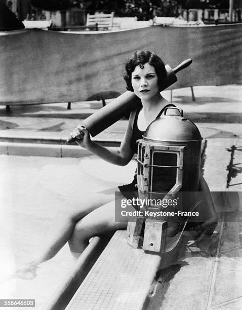 Jeune femme assise au bord d'une piscine à côté d'un casque de scaphandrier, circa 1930.