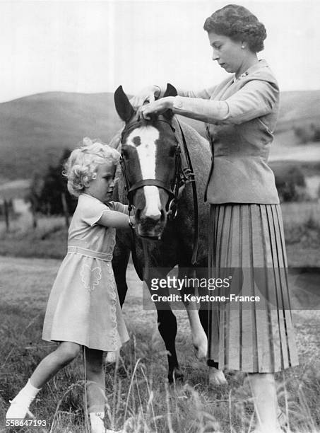 La Princesse Anne aide sa mere la Reine Elizabeth a ajuster les brides du poney dans le jardin du Chateau de Balmoral pendant leurs vacances d'ete en...