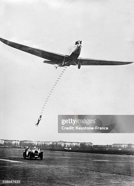 Un homme accroché par une échelle de corde à un avion en plein vol saute dans une automobile qui roule à 100 km/h, sur l'aérodrome de Tempelhof,...