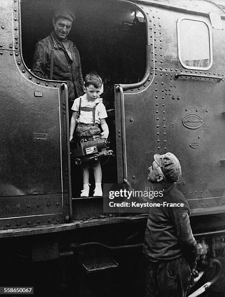 Petit garcon a bord d'une locomotive tenant un locomotive miniature a la main au moment des departs en vacances dans une gare, a Paris, France, le 2...