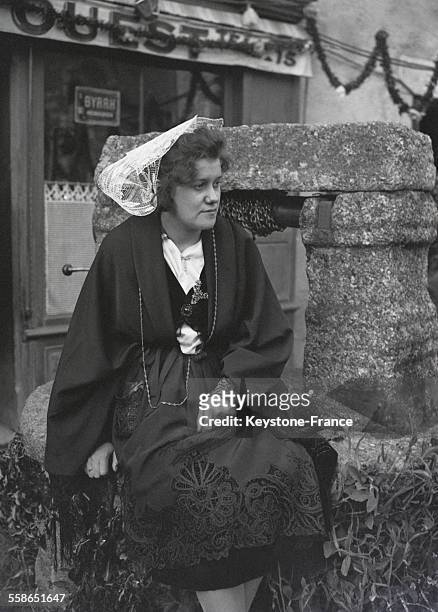 Portrait d'une bretonne en costume et coiffe traditionnels assise sur la margelle d'un puits en Bretagne, France, circa 1930.