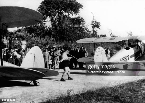Homme tirant un avion avec la machoire tout en s'arc-bouttant sur un autre appareil, à Lorient, France, circa 1930.