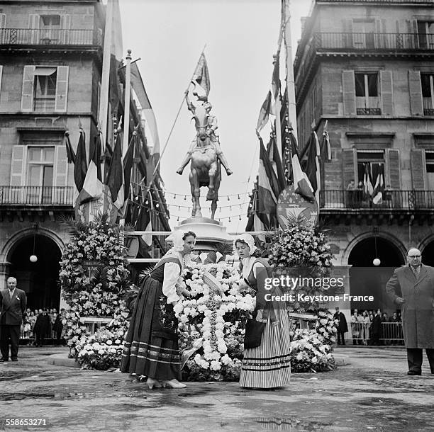 Deux jeunes filles habillées du vêtement traditionnel lorrain déposant une croix de Lorraine en fleurs au pied de la statue équestre de Jeanne d'Arc,...