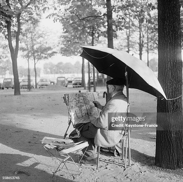 Dans le jardin bordant la Place de la Concorde et l'avenue des Champs-Elysées à Paris, France, un homme dessine au fusain, protègeant sa feuille des...